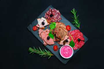 Antipasto platter cold meat with prosciutto, sausage, salami on slate stone board over marble background. Meat appetizer