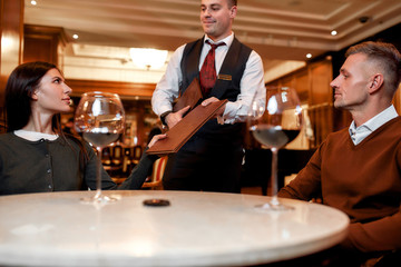 All about customers. Confident waiter giving menu to costumers. Couple having dinner in hotel restaurant