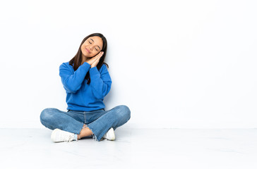 Young mixed race woman sitting on the floor isolated on white background making sleep gesture in dorable expression