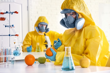 Scientist in chemical protective suit injecting orange at laboratory