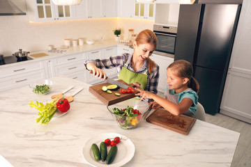 Mother and daughter cooking salad together in kitchen