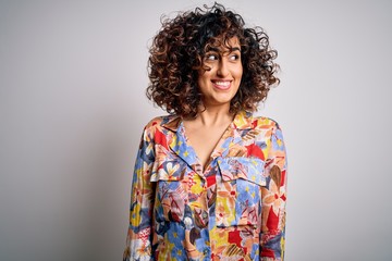 Young beautiful curly arab woman wearing floral colorful shirt standing over white background smiling looking to the side and staring away thinking.
