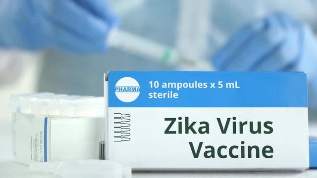 Box with zika virus vaccine on the table against blurred lab assistant or doctor. Fictional phaceutical logo