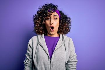 Beautiful curly arab sportswoman doing sport wearing sportswear over purple background afraid and shocked with surprise expression, fear and excited face.