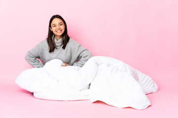 Young mixed race woman wearing pijama sitting on the floor posing with arms at hip and smiling