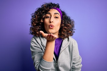 Beautiful curly arab sportswoman doing sport wearing sportswear over purple background looking at the camera blowing a kiss with hand on air being lovely and sexy. Love expression.