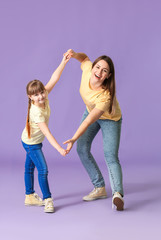 Happy mother and her little daughter dancing against color background