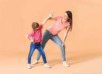 Happy mother and her little daughter dancing against color background