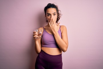 Young beautiful sportswoman with curly hair doing sport drinking glass of water cover mouth with...