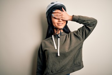 Young beautiful chinese woman wearing bike helmet over isolated white background smiling and laughing with hand on face covering eyes for surprise. Blind concept.
