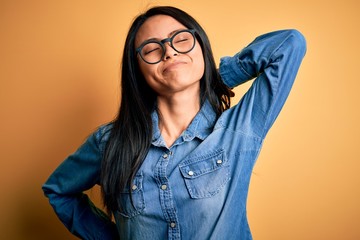 Young beautiful chinese woman wearing casual denim shirt over isolated yellow background Suffering of neck ache injury, touching neck with hand, muscular pain