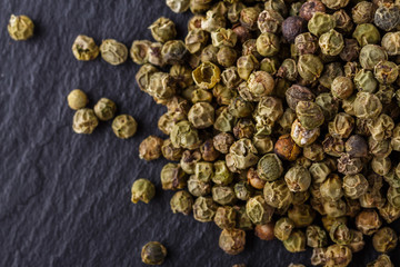 green peppercorns on dark slate stone background