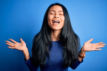 Young beautiful chinese woman wearing casual t-shirt over isolated blue background celebrating mad...