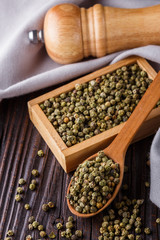 green peppercorns in wooden scoop on rustic background