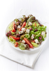 Healthy salad with feta cheese, various olives, leek and tomatoes. White wooden background. Copy space. 