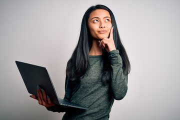 Young beautiful chinese woman using laptop standing over isolated white background serious face thinking about question, very confused idea