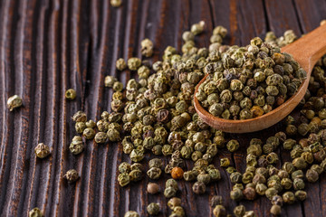 green peppercorns in wooden scoop on rustic background