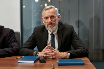 Confident businessman. Portrait of bearded mature man in formal wear looking at camera while sitting at the office table in the modern office