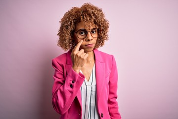 Young african american businesswoman wearing glasses standing over pink background Pointing to the eye watching you gesture, suspicious expression
