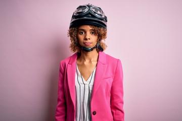 African american motorcyclist woman with curly hair wearing moto helmet over pink background depressed and worry for distress, crying angry and afraid. Sad expression.