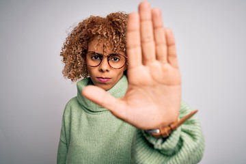 Young beautiful african american woman wearing turtleneck sweater and glasses doing stop sing with palm of the hand. Warning expression with negative and serious gesture on the face.