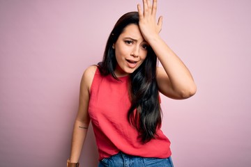 Young brunette woman wearing casual summer shirt over pink isolated background surprised with hand on head for mistake, remember error. Forgot, bad memory concept.