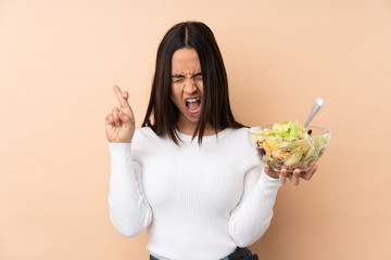 Young brunette girl holding a salad over isolated background with fingers crossing