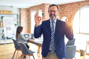 Middle age handsome businessman wearing glasses   standing at the office relax and smiling with eyes closed doing meditation gesture with fingers. Yoga concept.