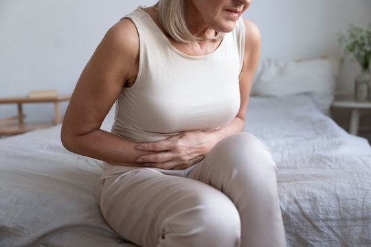 Cropped image older unhealthy woman embracing belly, suffering from strong stomach ache. Unhappy middle aged lady feeling discomfort in abdomen, pancreatitis gastritis diarrhea problem concept.