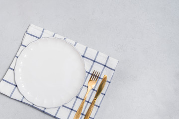 Cutlery background with white empty plate and golden knife and fork on neutral background