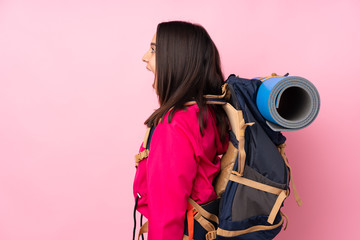 Young mountaineer girl with a big backpack over isolated pink background laughing in lateral position