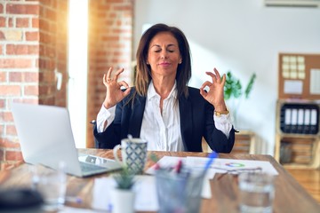 Middle age beautiful businesswoman working using laptop at the office relax and smiling with eyes closed doing meditation gesture with fingers. Yoga concept.