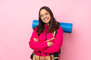 Young mountaineer girl with a big backpack over isolated pink background with glasses and happy