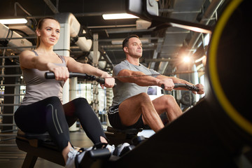 Low angle view at sportive couple using exercise machines during strength workout in modern gym,...