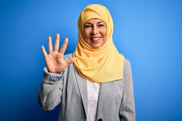 Middle age brunette business woman wearing muslim traditional hijab over blue background showing and pointing up with fingers number five while smiling confident and happy.