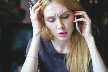 Beautiful blonde girl with serious expression solves business tasks and issues with mobile phone....