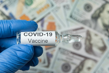 Ampoule with a vaccine from COVID-19 in the hand. Close-up. Money on the background. Pandemic Control Concept