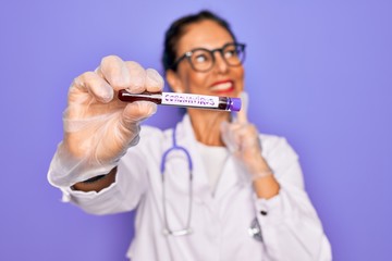 Middle age senior female doctor holding medice blood sample of coronavirus infection disease...