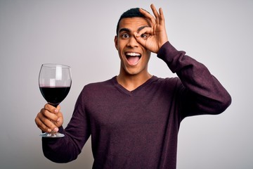 Handsome african american sommelier man tasting glass of red wine over white background with happy face smiling doing ok sign with hand on eye looking through fingers