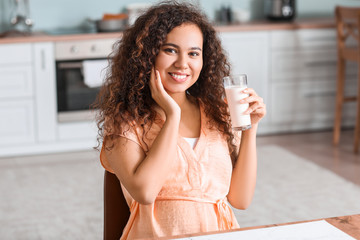 Young pregnant African-American woman with milk in kitchen