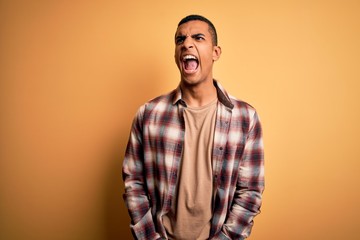 Obraz premium Young handsome african american man wearing casual shirt standing over yellow background angry and mad screaming frustrated and furious, shouting with anger. Rage and aggressive concept.