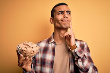 Young handsome african american man holding bowl with healthy cornflakes cereals serious face...