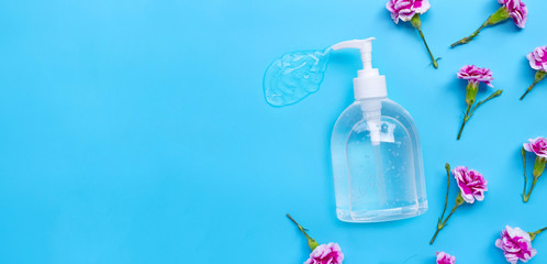 Alcohol hand sanitizer gel in pump bottle with carnation flower on blue background.