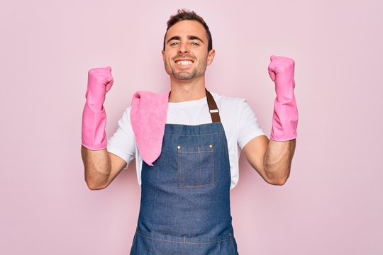 Young cleaner man with blue eyes cleaning wearing apron and gloves over pink background celebrating surprised and amazed for success with arms raised and open eyes. Winner concept.