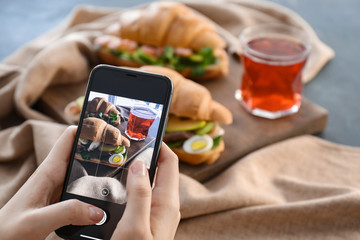 Woman taking photo of tasty croissant sandwiches on table