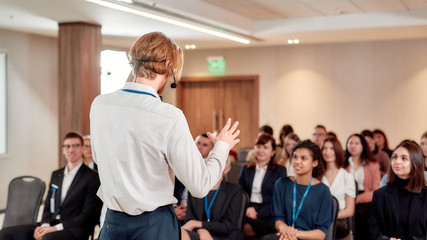 Where everyone gets a business education. Young male speaker in suit with headset giving a talk at business meeting