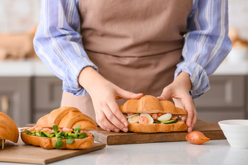 Obraz na płótnie Canvas Woman preparing tasty croissant sandwich in kitchen, closeup
