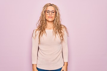 Obraz premium Young beautiful blonde woman wearing casual sweater and glasses over pink background Relaxed with serious expression on face. Simple and natural looking at the camera.