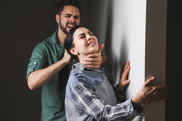 Angry husband trying to kill his wife indoors. Concept of domestic violence