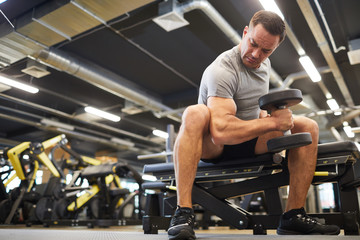Fototapeta na wymiar Low angle full length portrait of mature muscular man doing exercises with dumbbells during strength workout in modern gym, copy space